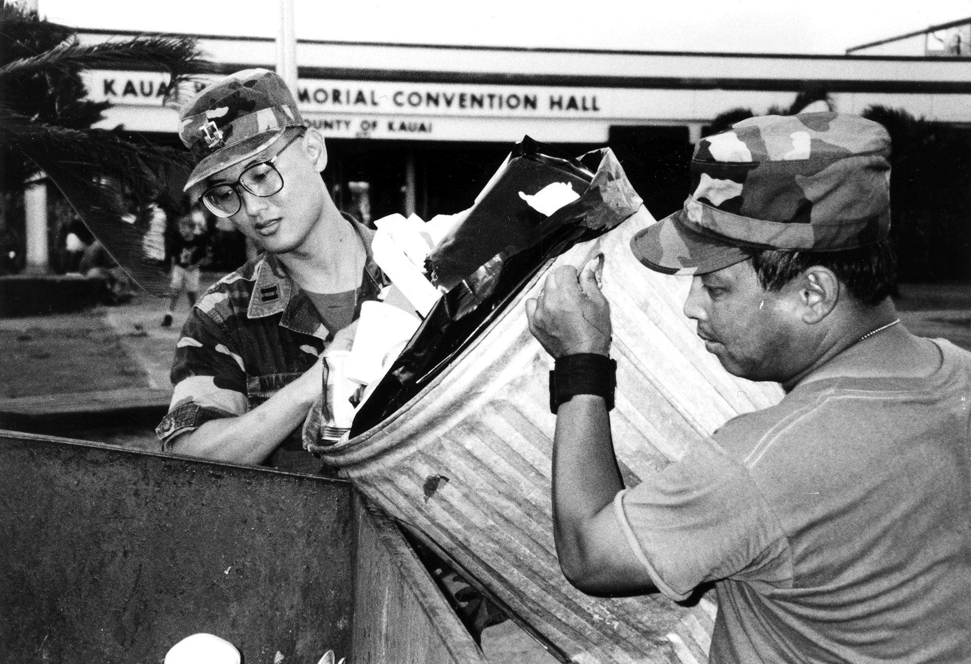 After Hurricane Iniki hit the island of Kauai in September 1992, the Hawaii National Guard mobilized to assist in the island's recovery efforts. This photograph shows then-CPT Paul Nanamori and an unidentified soldier dumping trash outside the Kauai War Memorial Convention Hall.