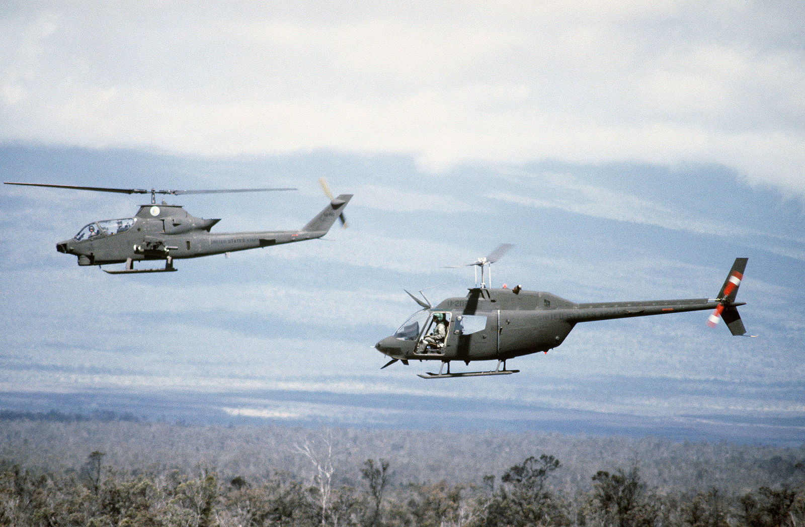 A left side view of an AH-1 Cobra helicopter, front, and an OH-58 Kiowa helicopter flying in formation during Exercise OPPORTUNE JOURNEY 85-3. Both helicopters are from the 19th Air Cavalry, Hawaii Army National Guard.
