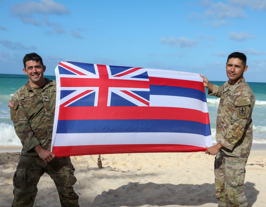 Hawaii Army National Guard Spc. Quinn Mears, left, a combat engineer assigned to Alpha Company, 227th Brigade Engineering Battalion and Hawaii Army National Guard Sgt. Cooper Hulse, a cavalry scout assigned to Headquarters and Headquarters Squadron, 1-299th Cavalry Regiment, poses for a photo with the Hawaiian Flag after the Beach Party event of the Region VII Best Warrior Competition, Waimanalo, Hawaii, May 7-11 2023. National Guard service members from Arizona, California, Colorado, Guam, Hawaii, Nevada, New Mexico and Utah competed against each other in Army Warrior Tasks to be named Regional Best Warrior. (U.S. Army National Guard photo by Spc. Sean Walker)