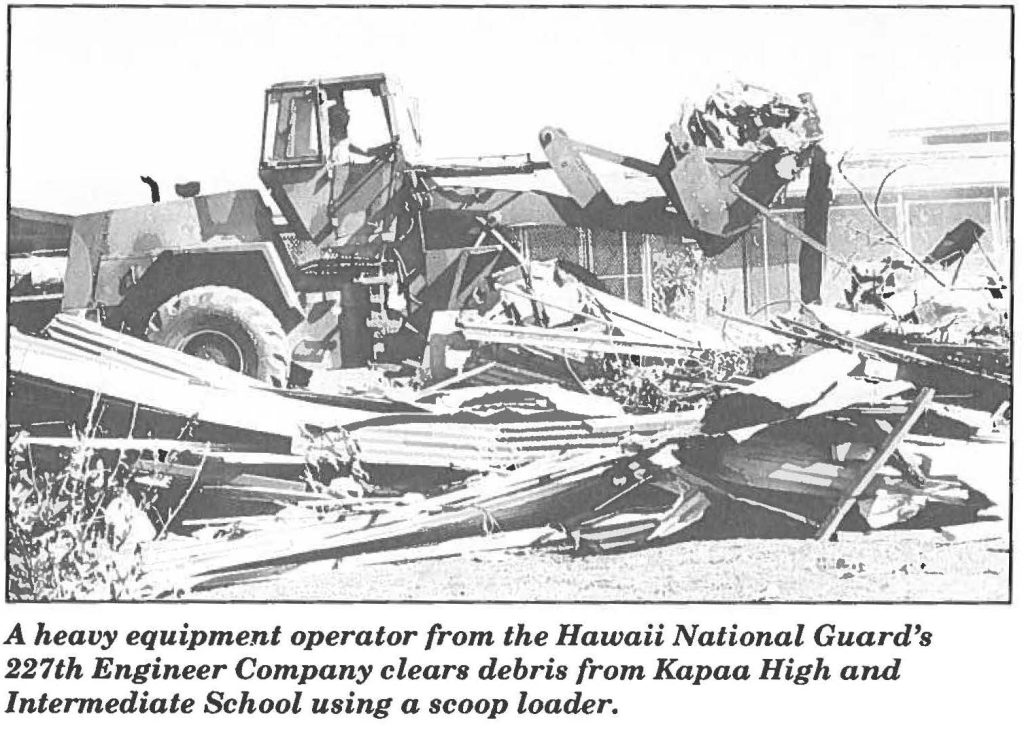 A heavy equipment operator from the Hawaii National Guard's 227th Engineer Company clears debris from Kapaa High and Intermediate School using a scoop loader.
