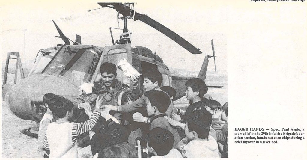 EAGER HANDS - Spec. Paul Asato, a crew chief in the 29th Infantry Brigade's aviation section, hands out corn chips during a brief layover in a river bed.