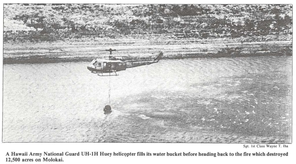 A Hawaii Army National Guard UH-1H Huey helicopter fills its water bucket before heading back to the fire which destroyed 12,500 acres on Molokai.