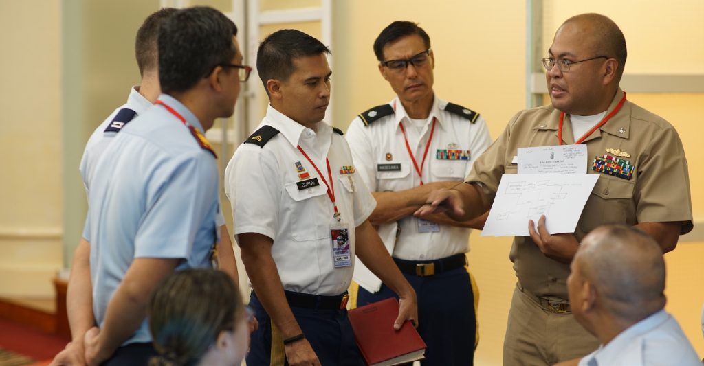 U.S. Navy Commander, Theodore Quidem discusses information operations with a working group of military staff planners first full day of planning at Gema Bhakti, Sept. 19, 2018, Jakarta Indonesia. Gema Bhakti is a joint force multi-national staff exercise where military staff from the U.S. Indo-Pacific Command and Indonesia work through a process known as the military decision making process. This process is a crucial step that involves the commander’s staff working with with all the higher and lower commands to define the mission, its variables, and the situation involved and how to measure mission effectiveness before a plan or order is produced. (U.S. Air National Guard Photo by Tech. Sgt. Andrew Jackson)